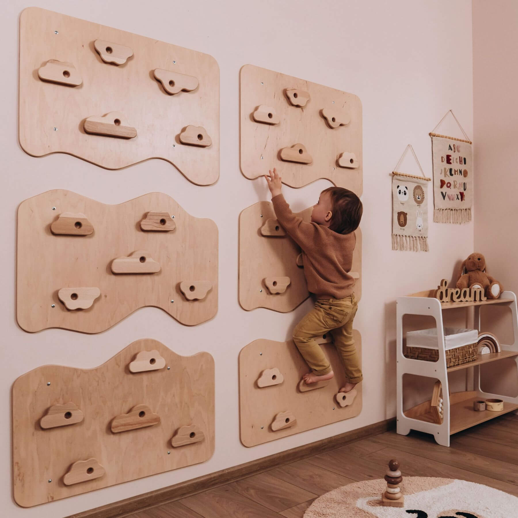 Child climbing on a wooden climbing wall in a room with toys and furniture.
