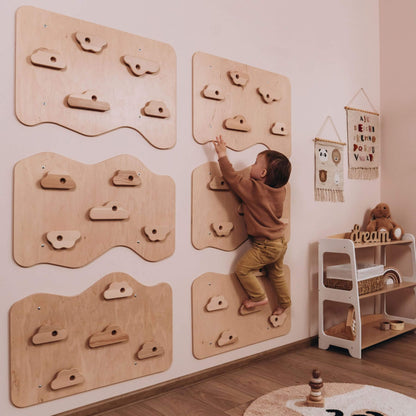Child climbing on a wooden climbing wall in a room with toys and furniture.
