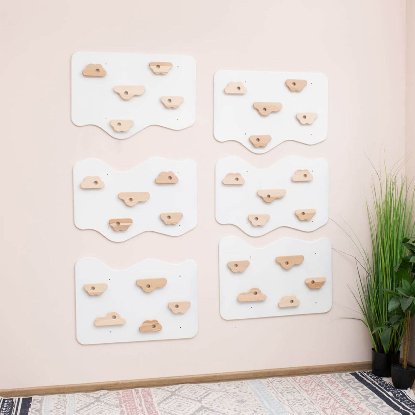 Set of wooden climbing holds on white panels against a light pink wall.