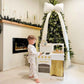 Child playing with Tiny Land® Honey Kitchenette - Little Chef's First Kitchen in a room with a Christmas tree and fireplace.