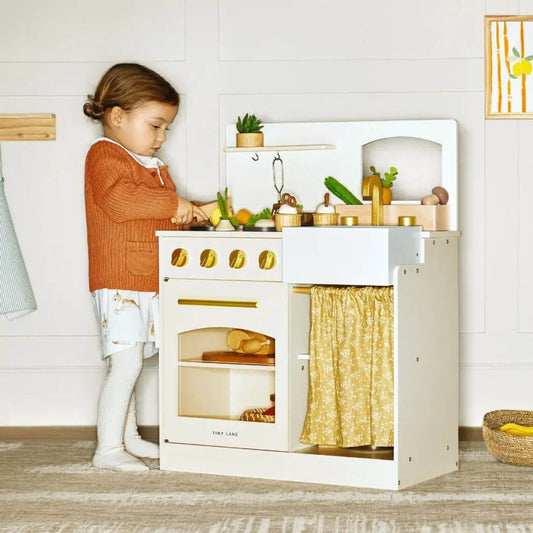 Child playing with Tiny Land® Honey Kitchenette - Little Chef's First Kitchen in a room with a white wall and wooden floor.