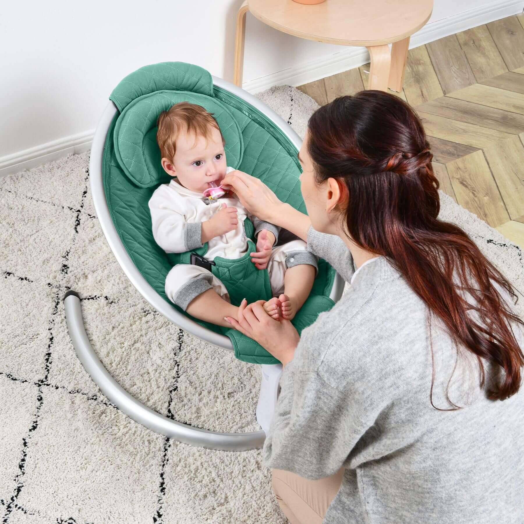 Woman holding a baby in Hot Mom Electric Baby Bouncer for Infant - Green on a carpeted floor.