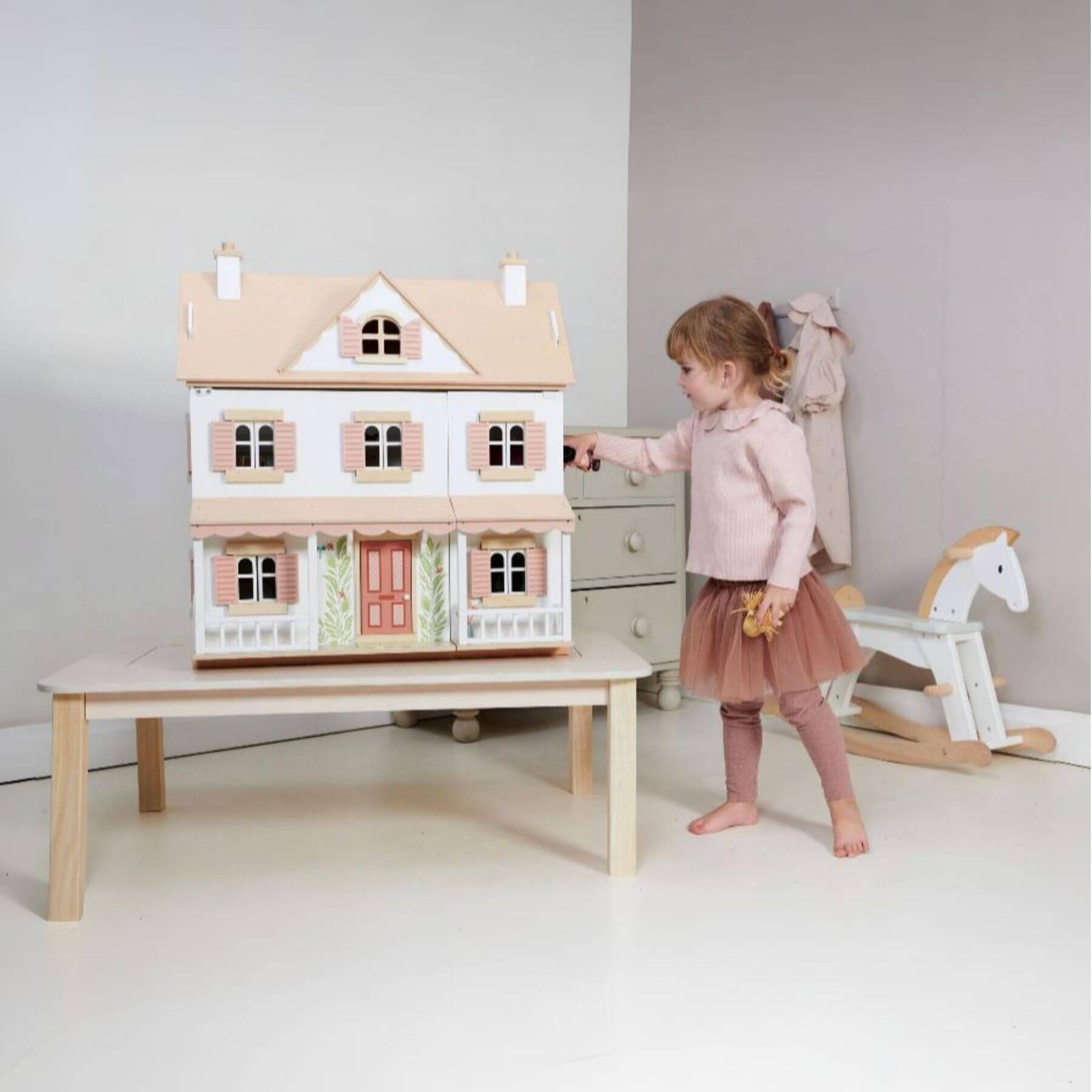 Child playing with Tender Leaf Humming Bird House on a table in a room with a rocking horse.