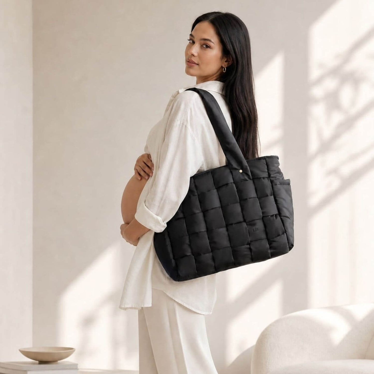 A pregnant woman in a white outfit carries Luli Bebé Infinite Diaper Bag - Black