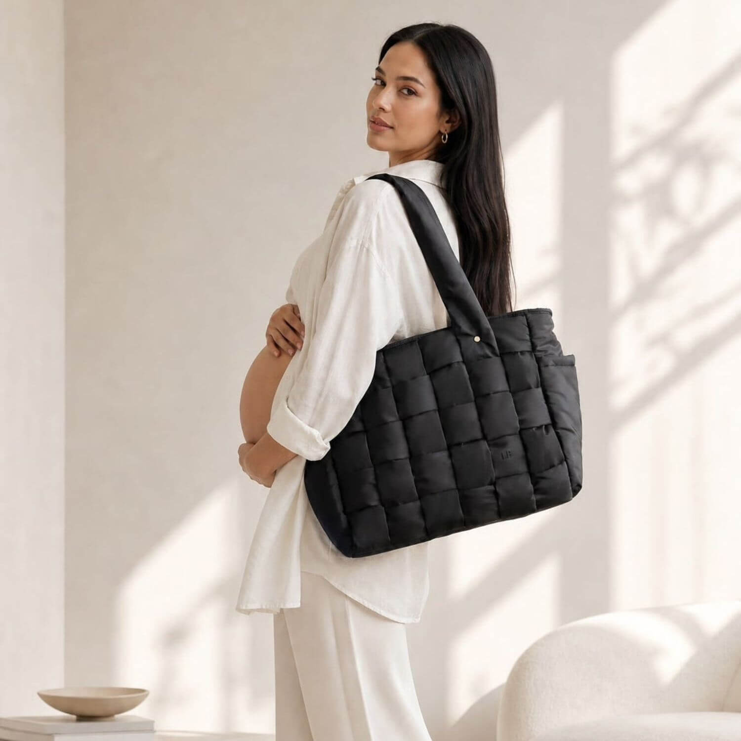 A pregnant woman in a white outfit carries Luli Bebé Infinite Diaper Bag - Black