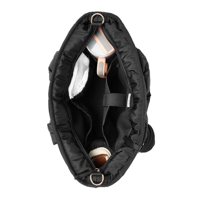 An overhead view of an open Luli Bebé Infinite Diaper Bag - Black showing its interior compartments, lining, and storage pockets, with a white and rose gold item visible inside, set against a plain white background.