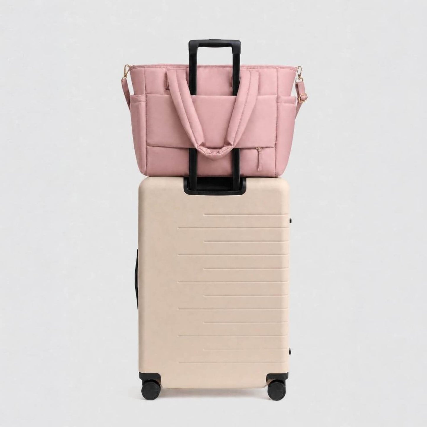 Luli Bebé Infinite Diaper Bag - Blush sits on top of a cream-colored hardshell rolling suitcase against a light gray background.