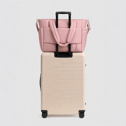 Luli Bebé Infinite Diaper Bag - Blush sits on top of a cream-colored hardshell rolling suitcase against a light gray background.