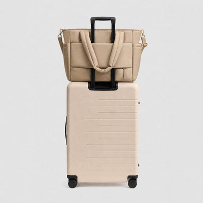 Luli Bebé Infinite Diaper Bag - Latte, stacked on top of a matching beige hard-shell rolling suitcase against a light gray studio background.