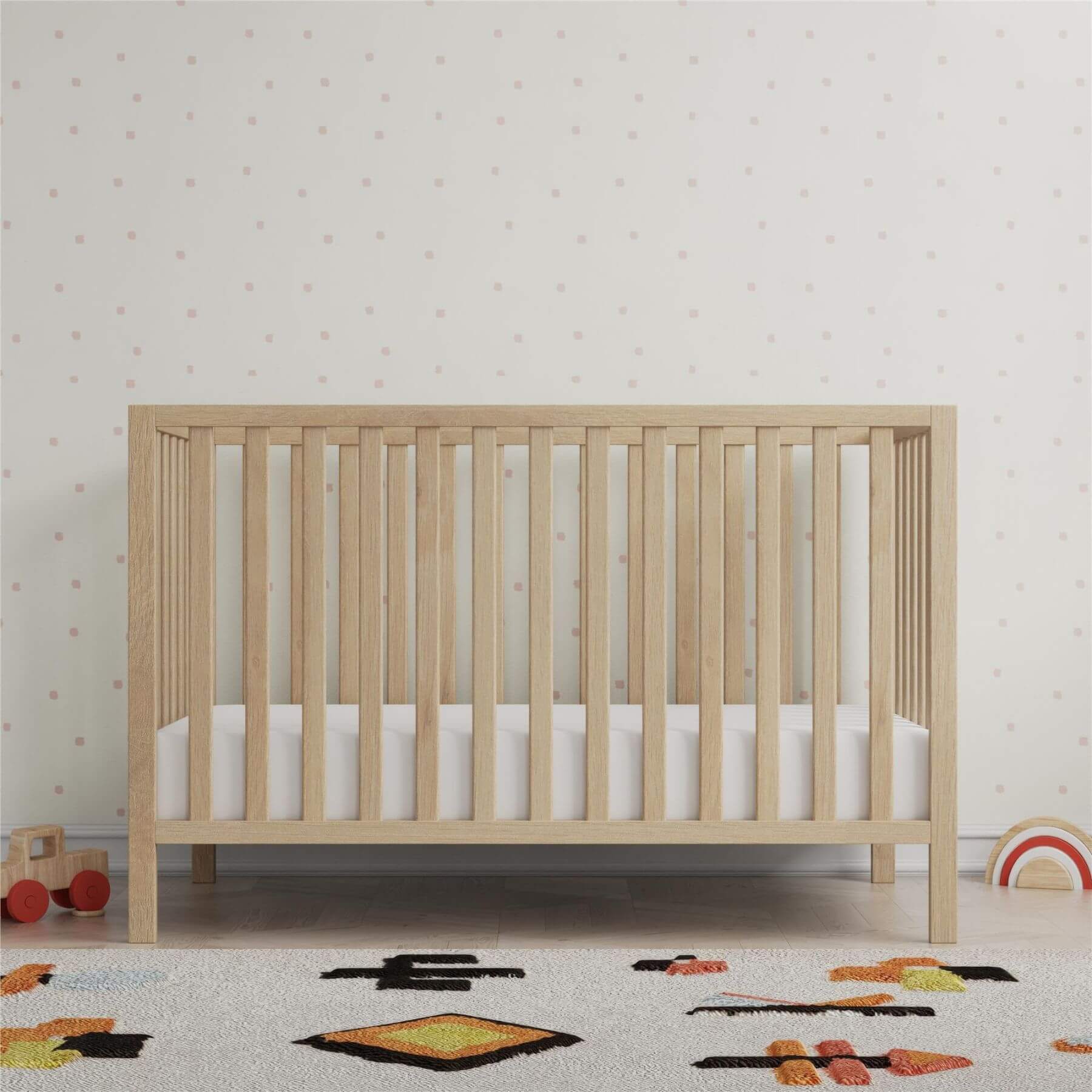 Ivey 3-in-1 Convertible Crib Light Natural with white mattress in a room with toys and patterned wallpaper