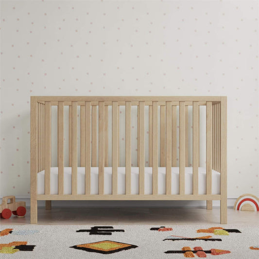 Ivey 3-in-1 Convertible Crib Light Natural with white mattress in a room with toys and patterned wallpaper
