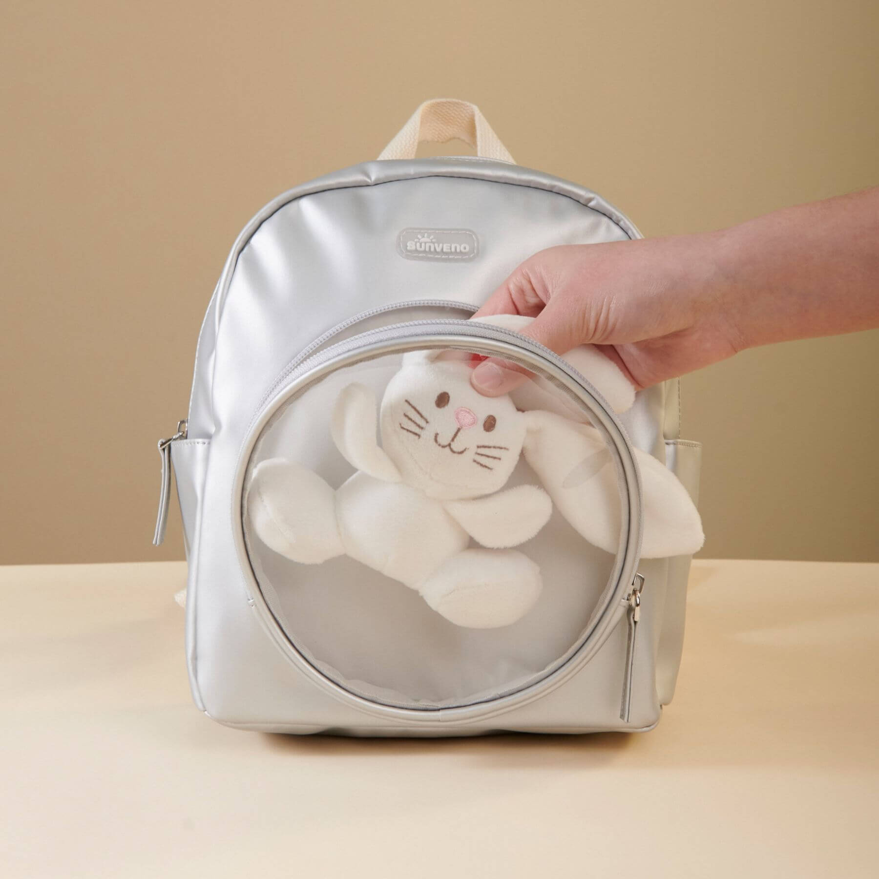 Sunveno Jelly Adventure Backpack - Silver with a clear front pocket containing a plush toy, on a beige background