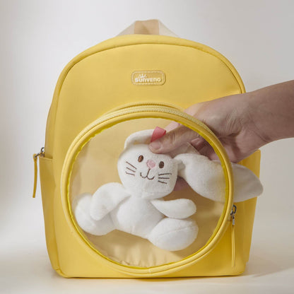 Yellow backpack with a clear front pocket containing a white plush toy, held by a hand.