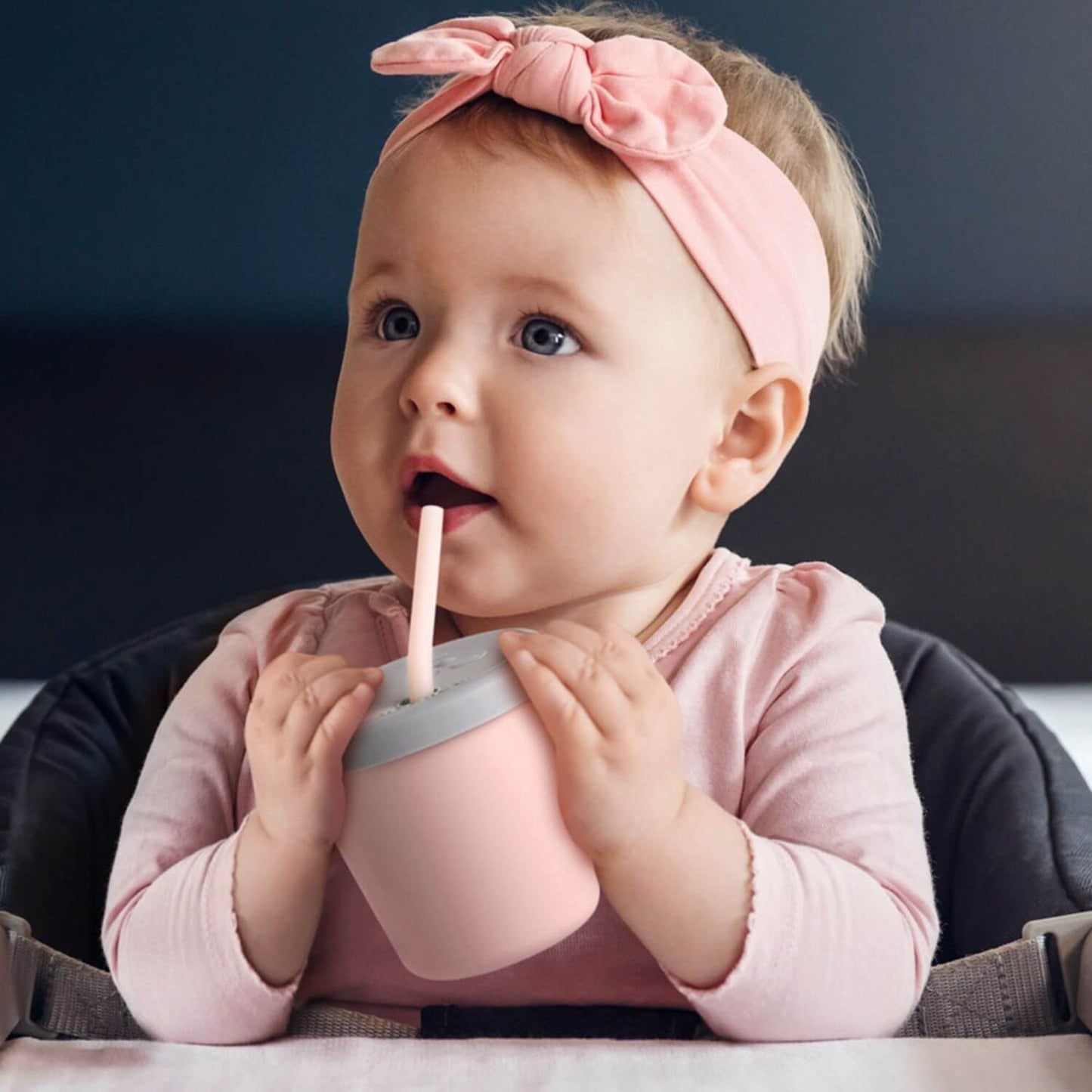 Baby in a pink outfit with a bow headband drinking from Haakaa Jolly Hippo Silicone Sippy Cup