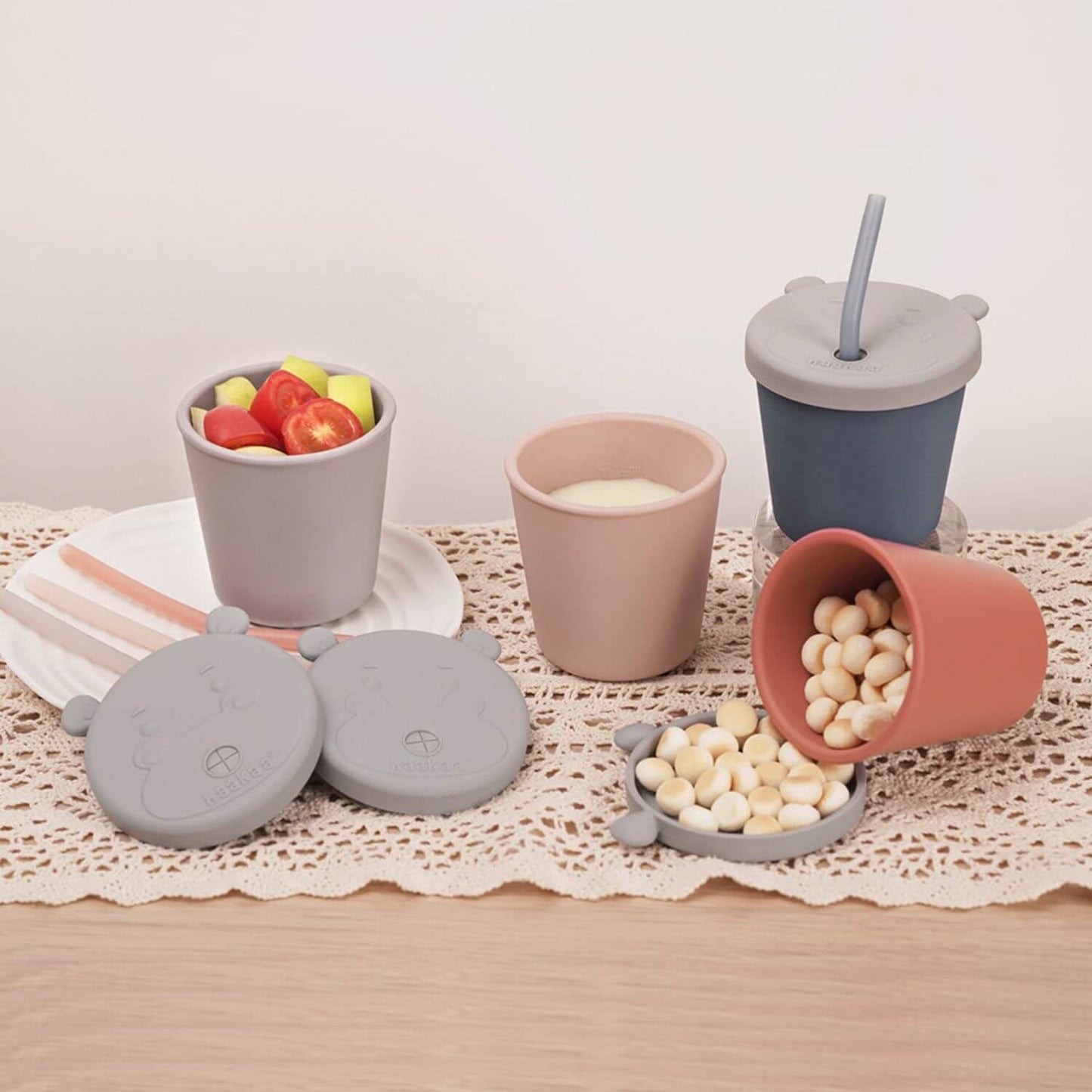 Set of silicone snack cups with lids on a lace tablecloth.