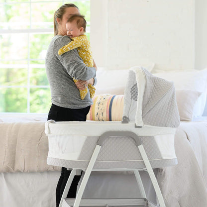 Mom Holding Baby next to TruBliss Journey 3-in-1 Bassinet