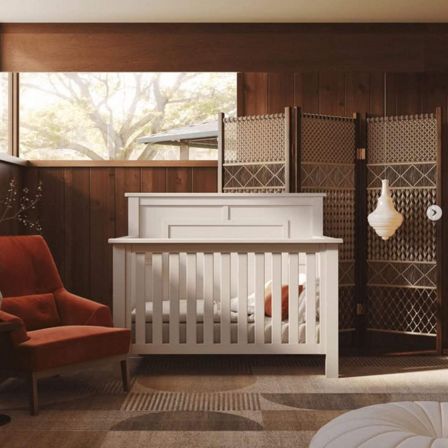 White crib in a room with wooden walls and a red armchair.