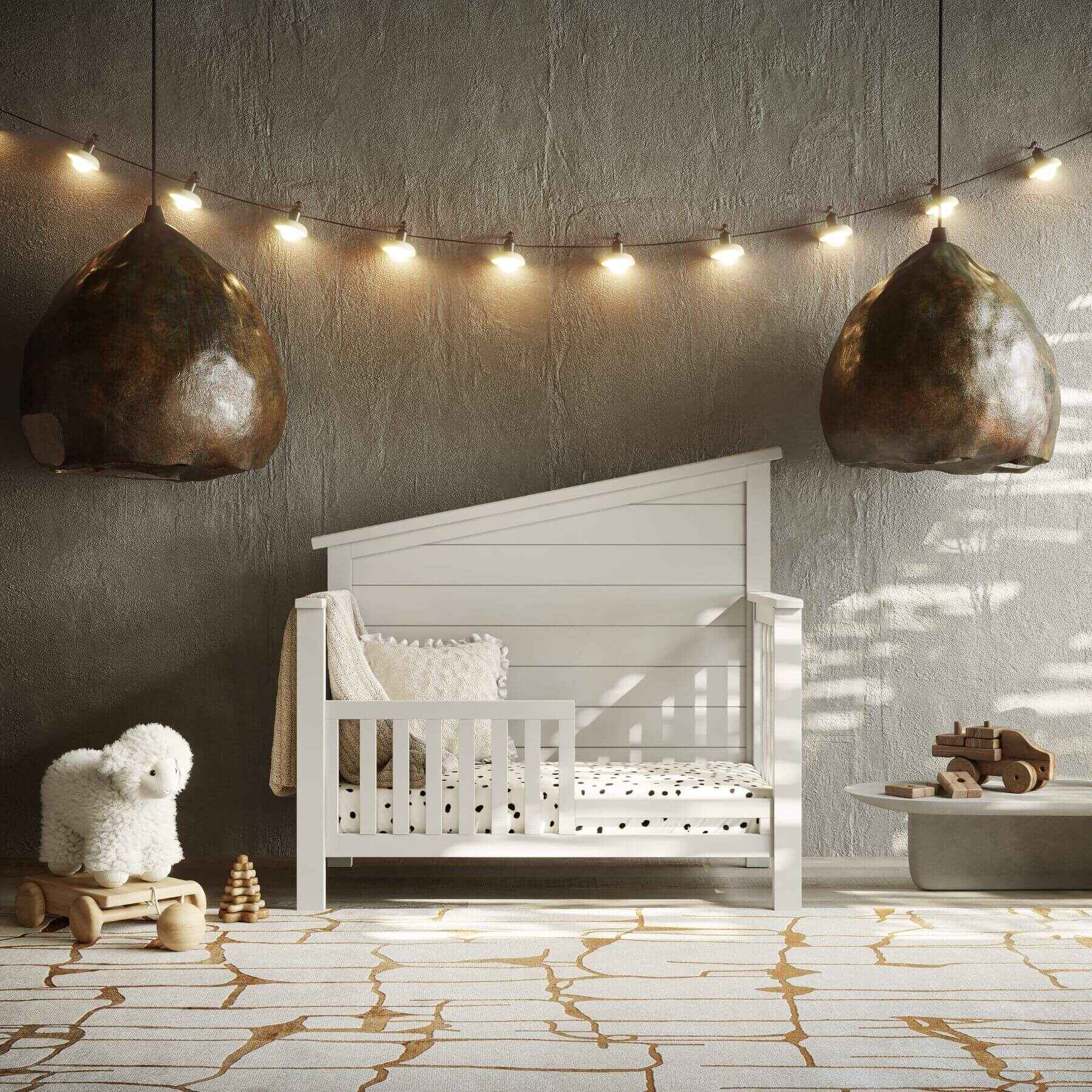 Nursery room with "Just White"  Balanced Baby Convertible Crib, toys, and string lights on a textured wall.