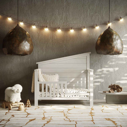 Nursery room with "Just White"  Balanced Baby Convertible Crib, toys, and string lights on a textured wall.