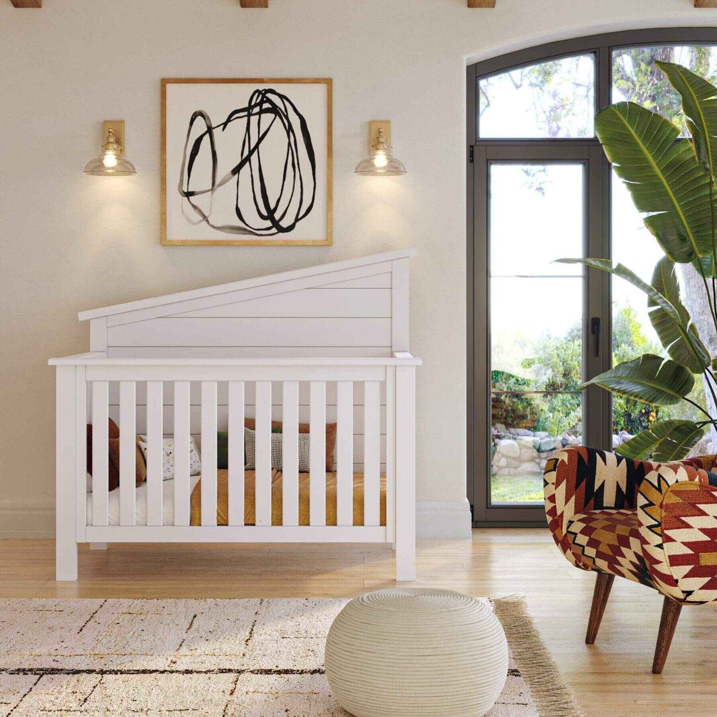 "Just White"  Balanced Baby Convertible Crib in a room with abstract art, a chair, and a plant.