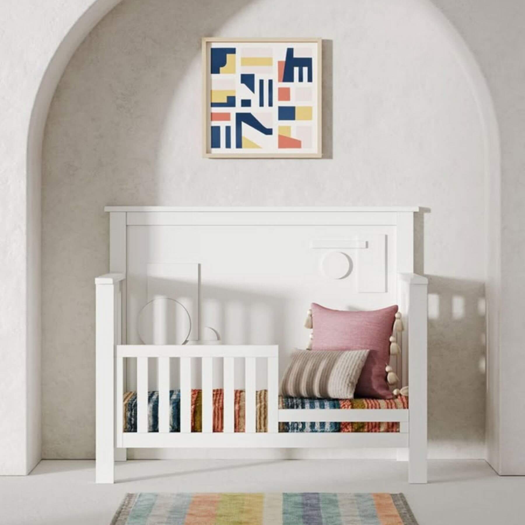 White crib with colorful bedding and a abstract art piece on the wall.