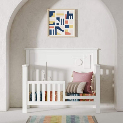White crib with colorful bedding and a abstract art piece on the wall.
