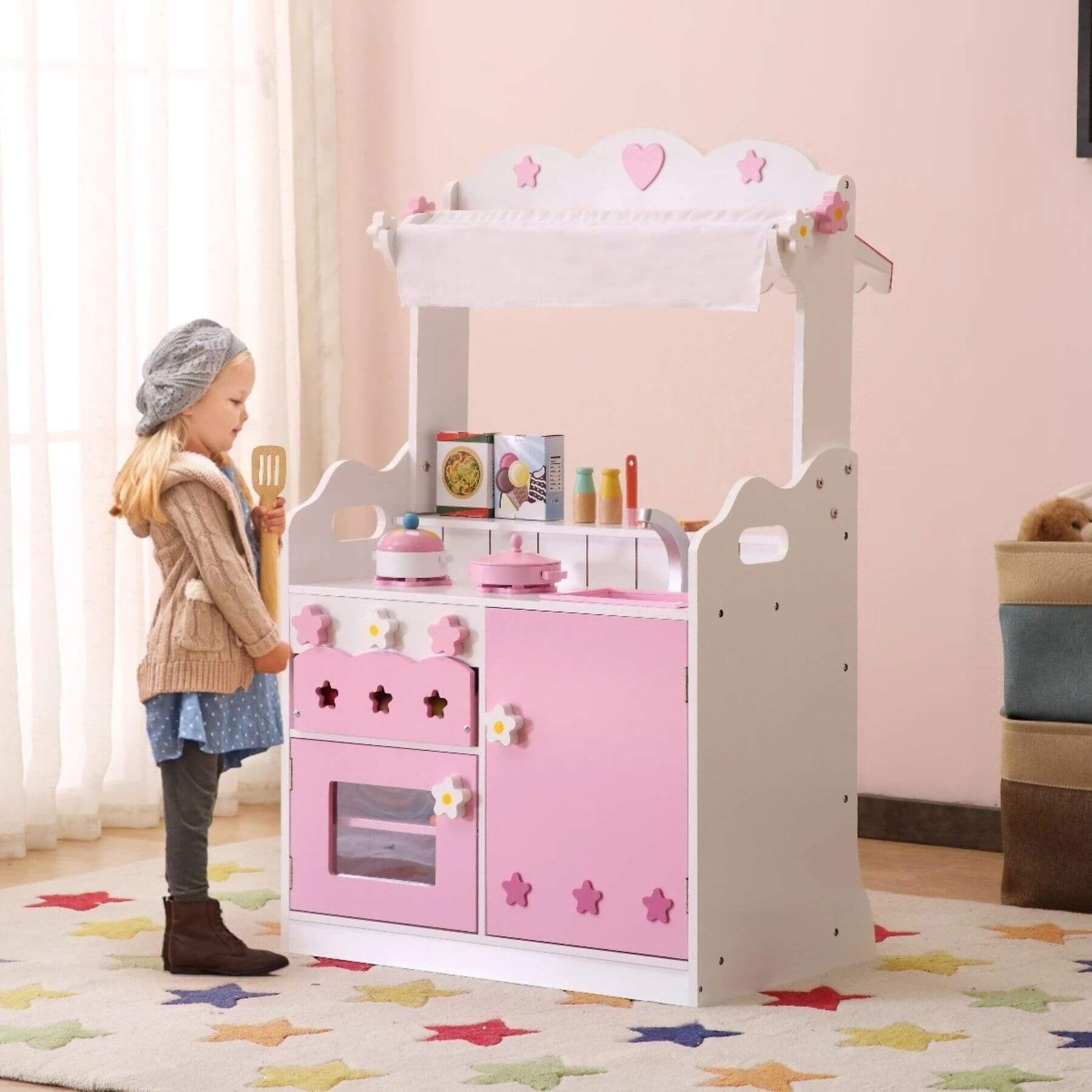 Child playing with Kids Funnel 2 In 1 Pink Pretend Kitchen and Market Stall in a room with a pink wall and colorful rug.