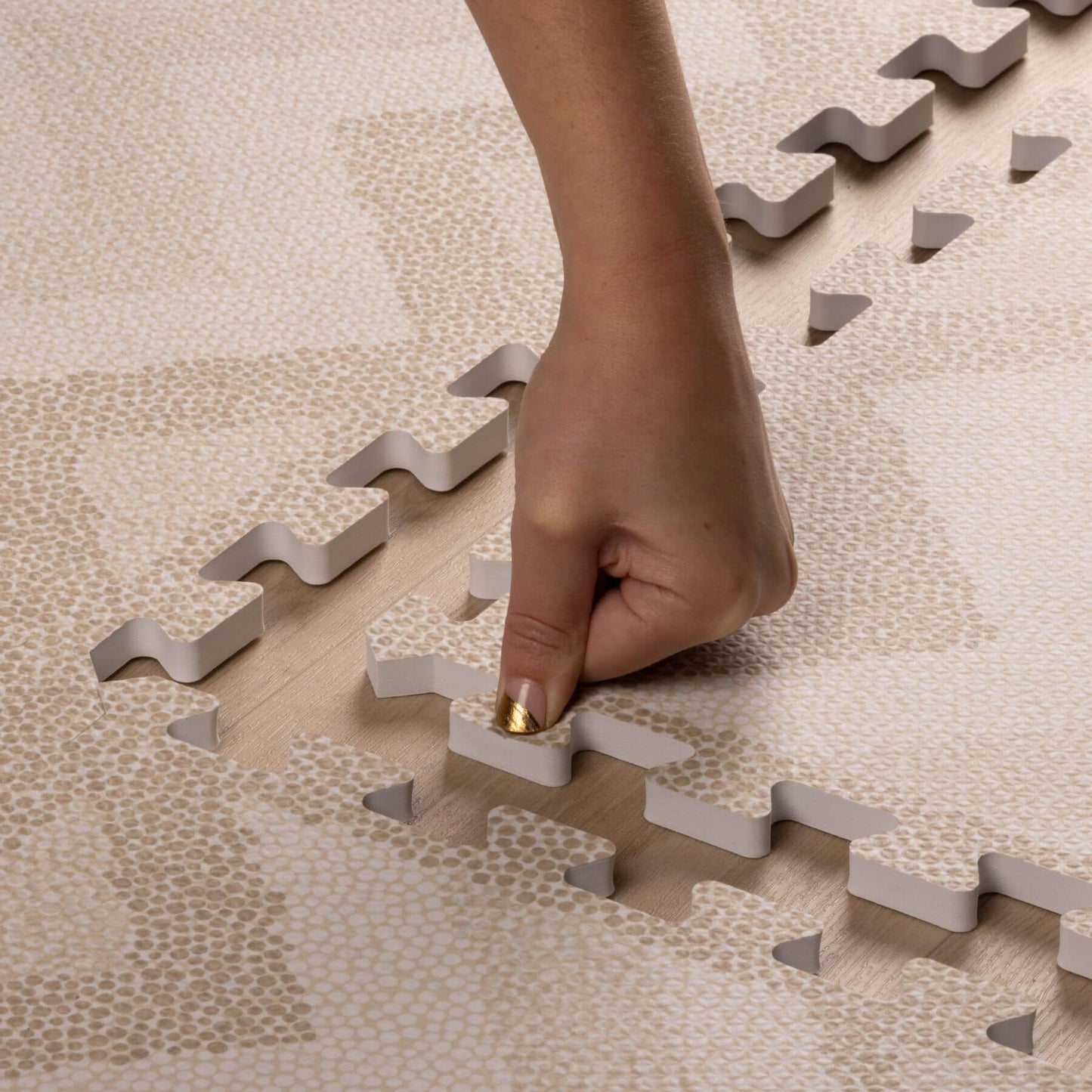 Hand placing a puzzle piece on a beige interlocking foam mat