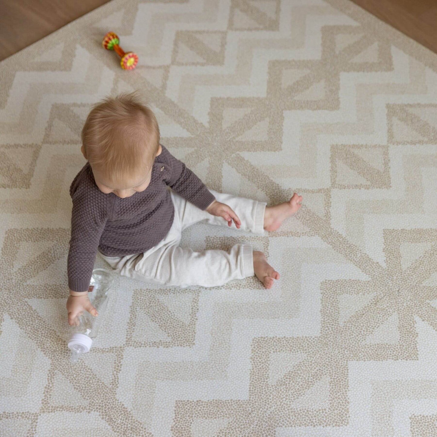 Baby sitting on Eeveve Kilim Play Mat - Soft Beige holding a bottle