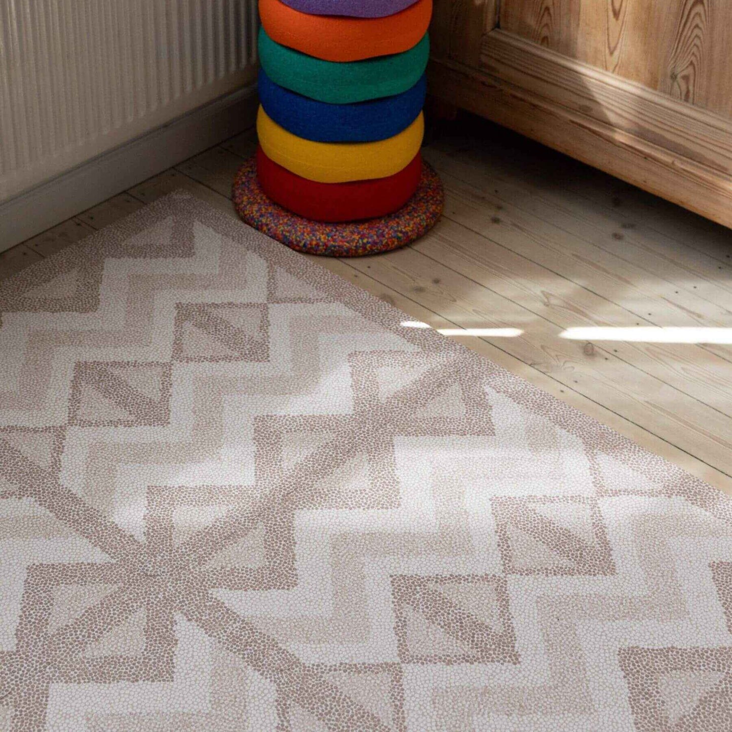 Eeveve Kilim Play Mat - Warm Pink on a wooden floor, next to a colorful cylindrical object.