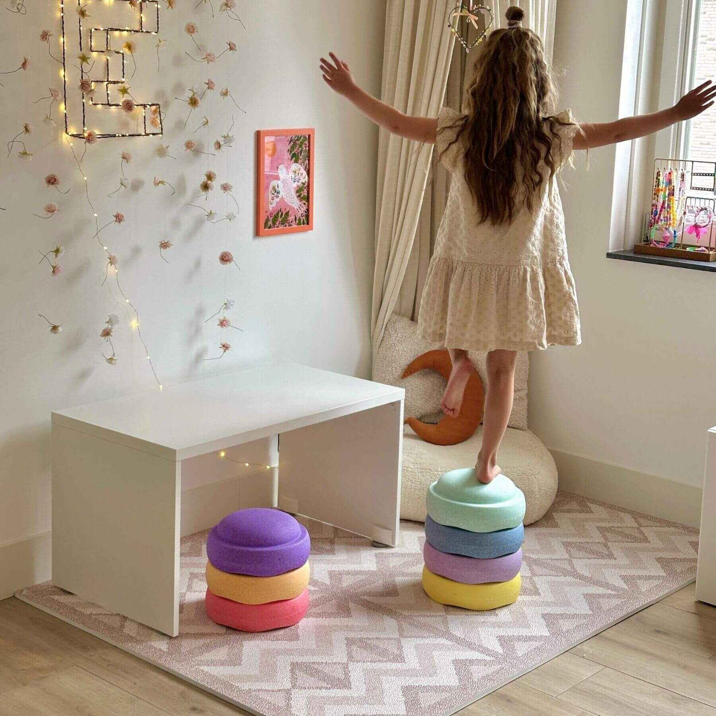 Child playing with colorful stacking toys in a room with a white table and decorative elements.