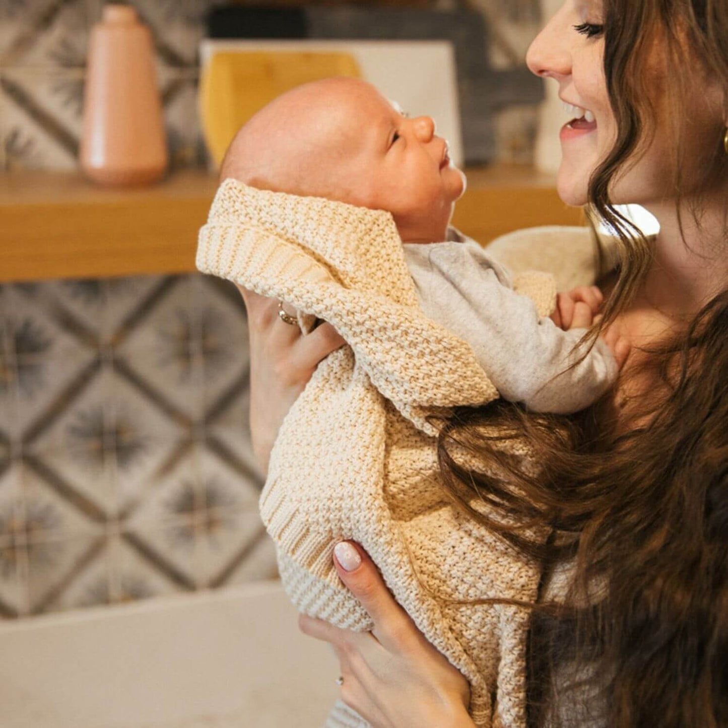 Mom Holding Baby Wrapped in Plum+Sparrow Knitted Blanket Macadamia