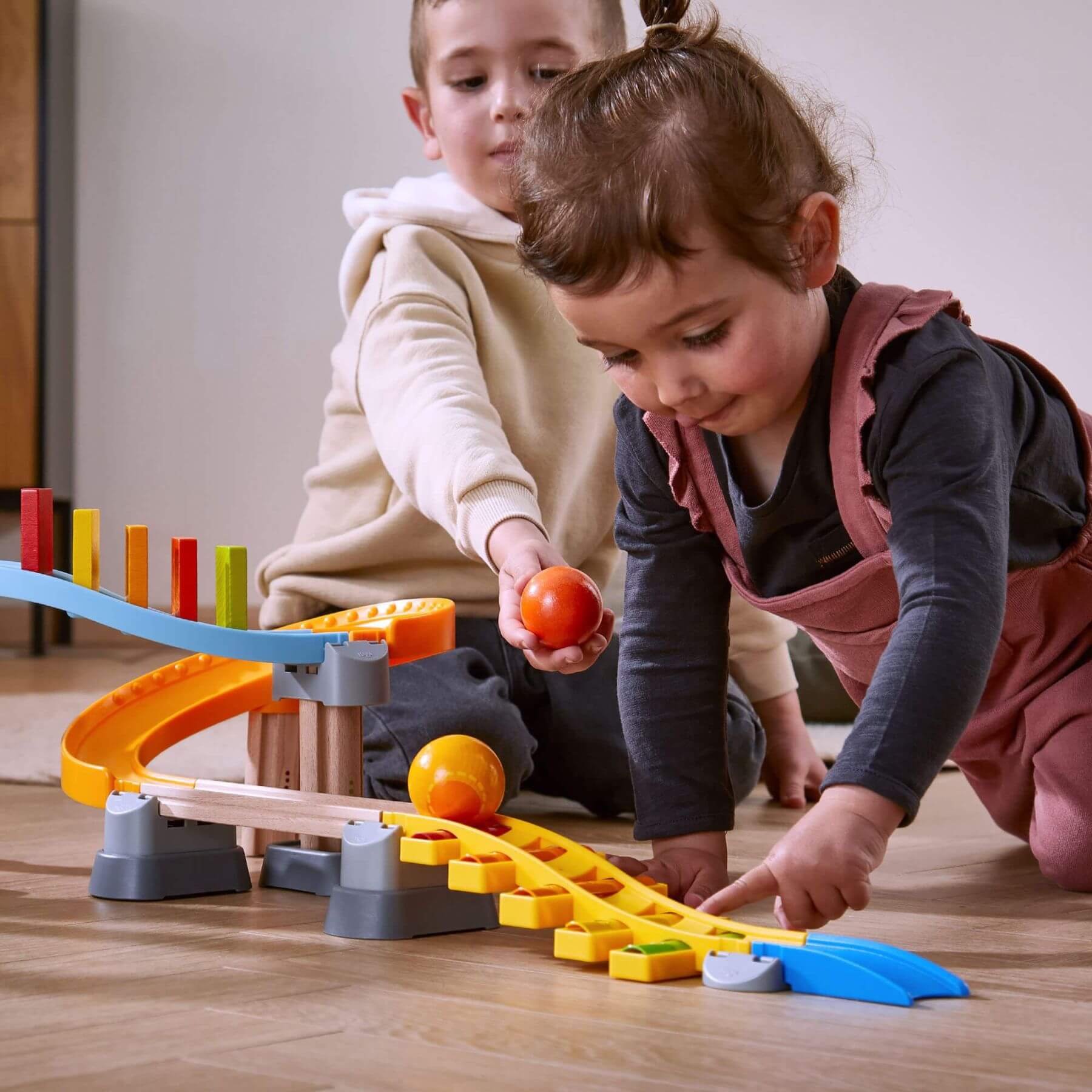 Two children playing with HABA USA Kullerbu Melody Dominoes Set on a wooden floor.