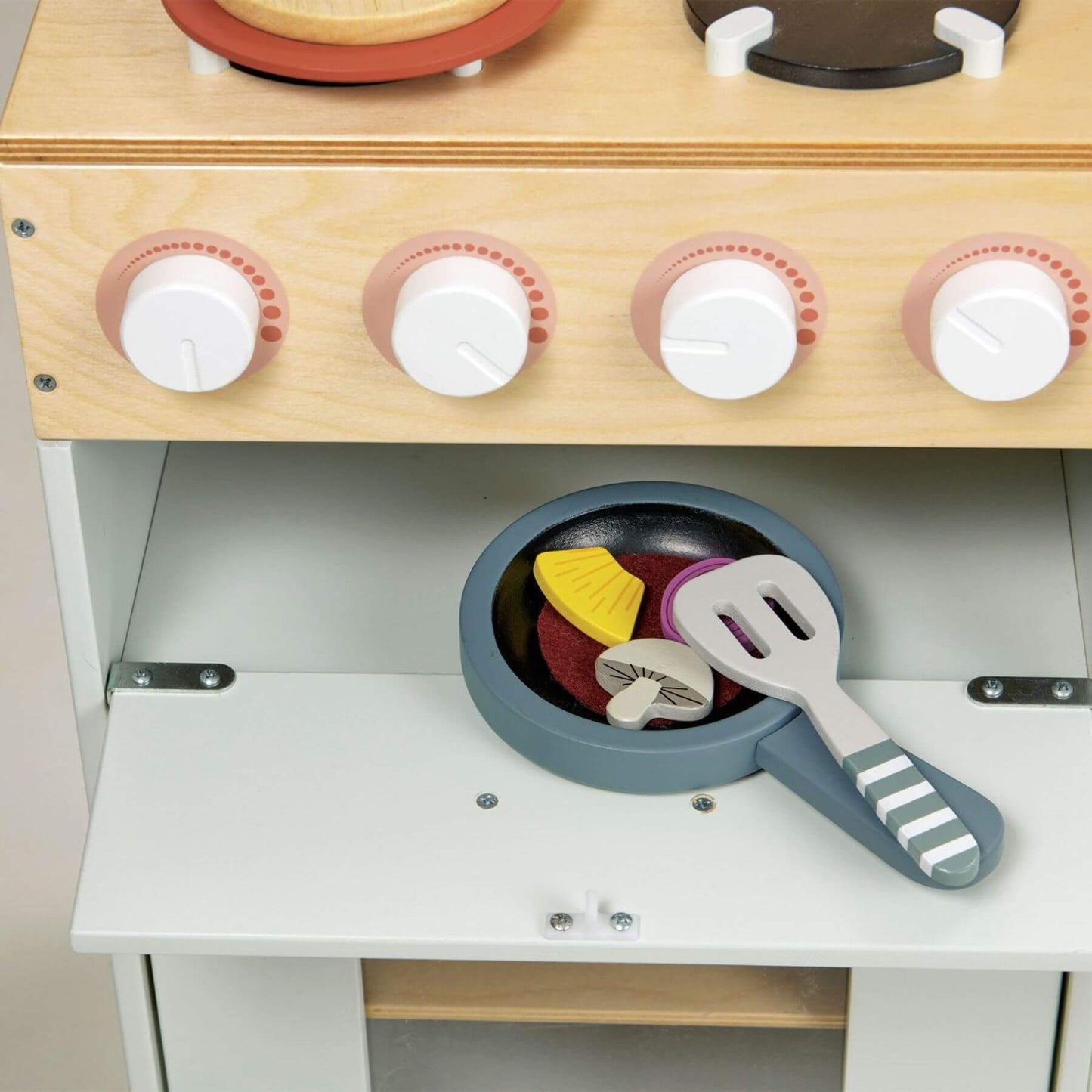 Wooden toy kitchen set with a stove, pan, and utensils on a neutral background