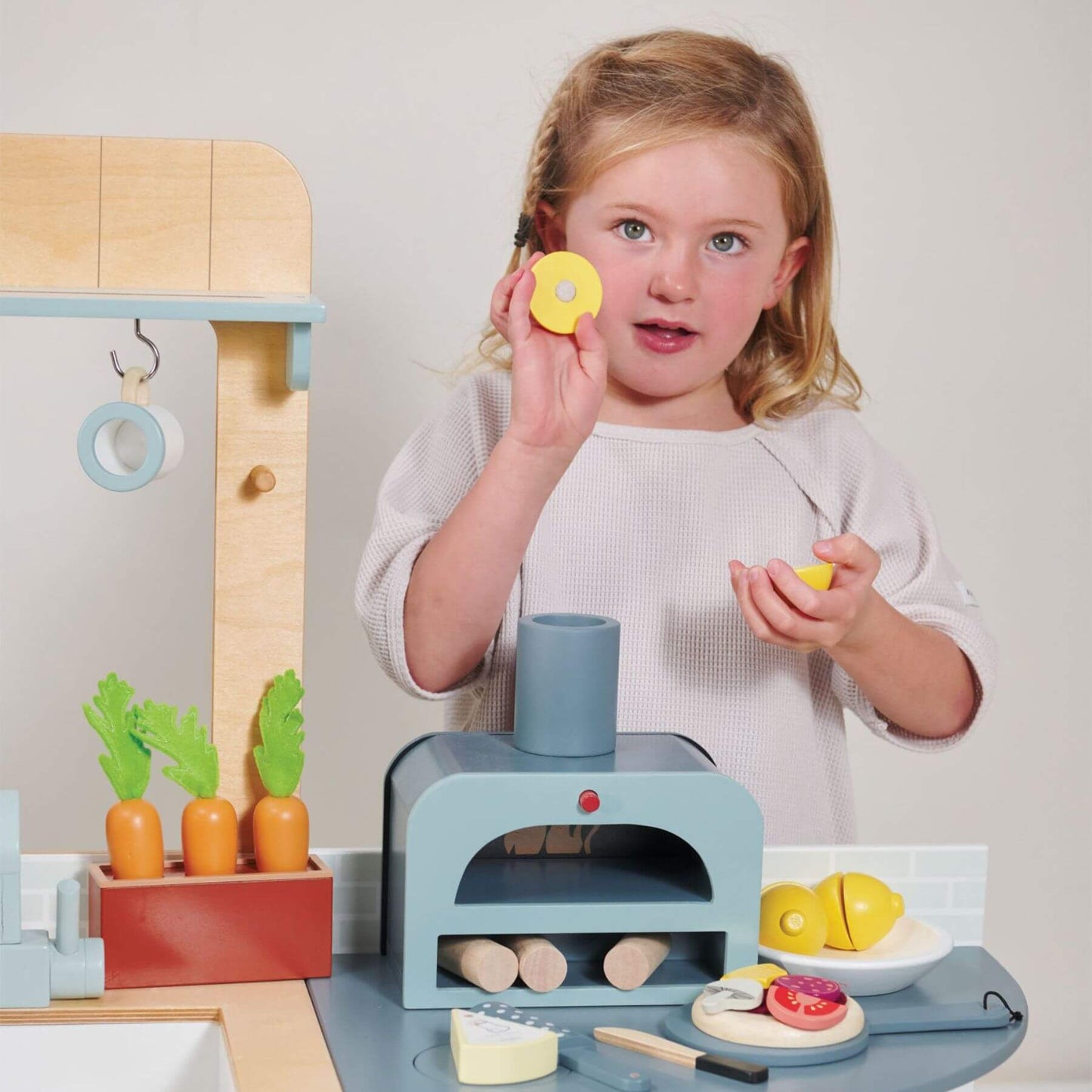 Child playing with Tender Leaf La Fiamma Grand Kitchen, holding toy food items.