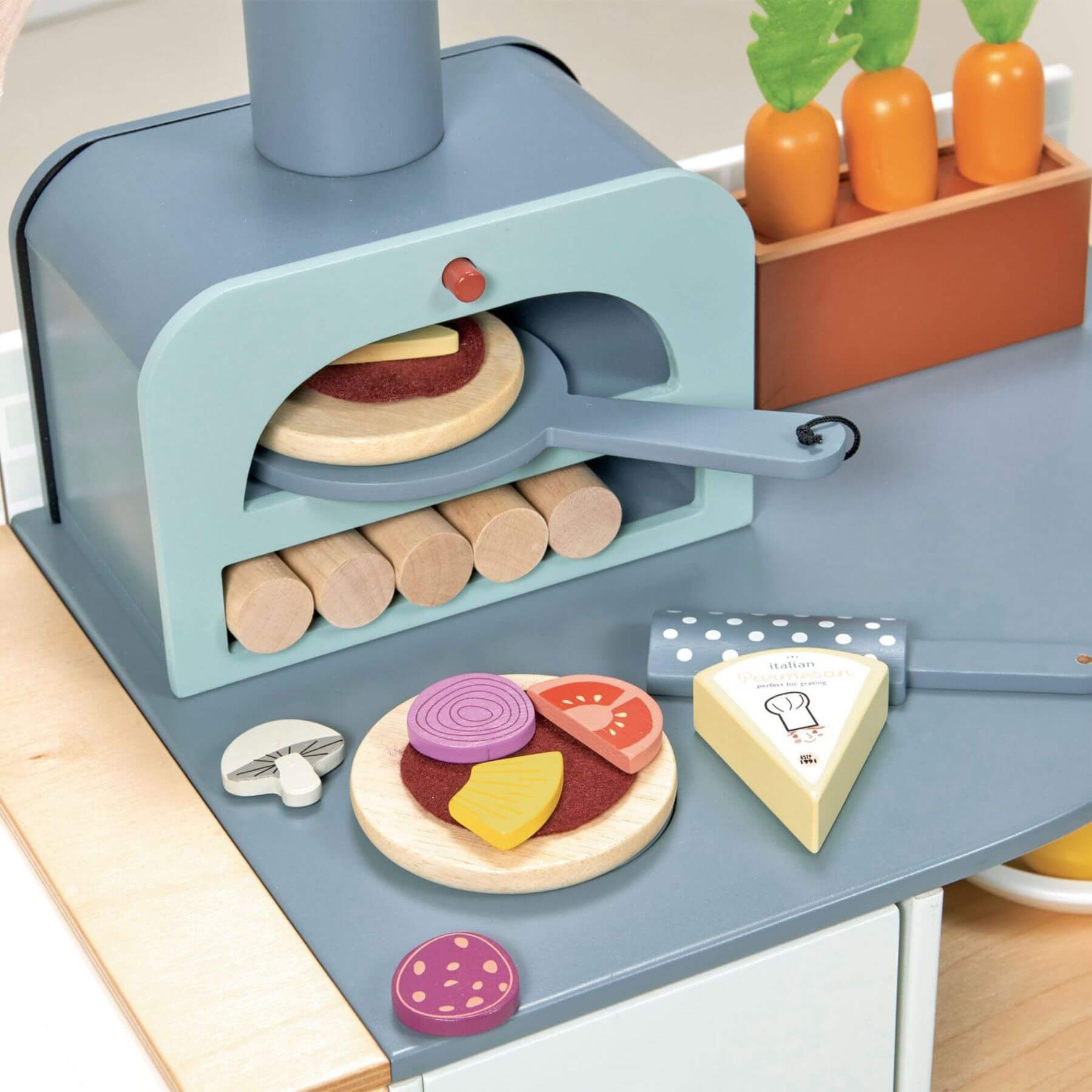 Toy pizza oven with wooden pizza and ingredients on a kitchen counter