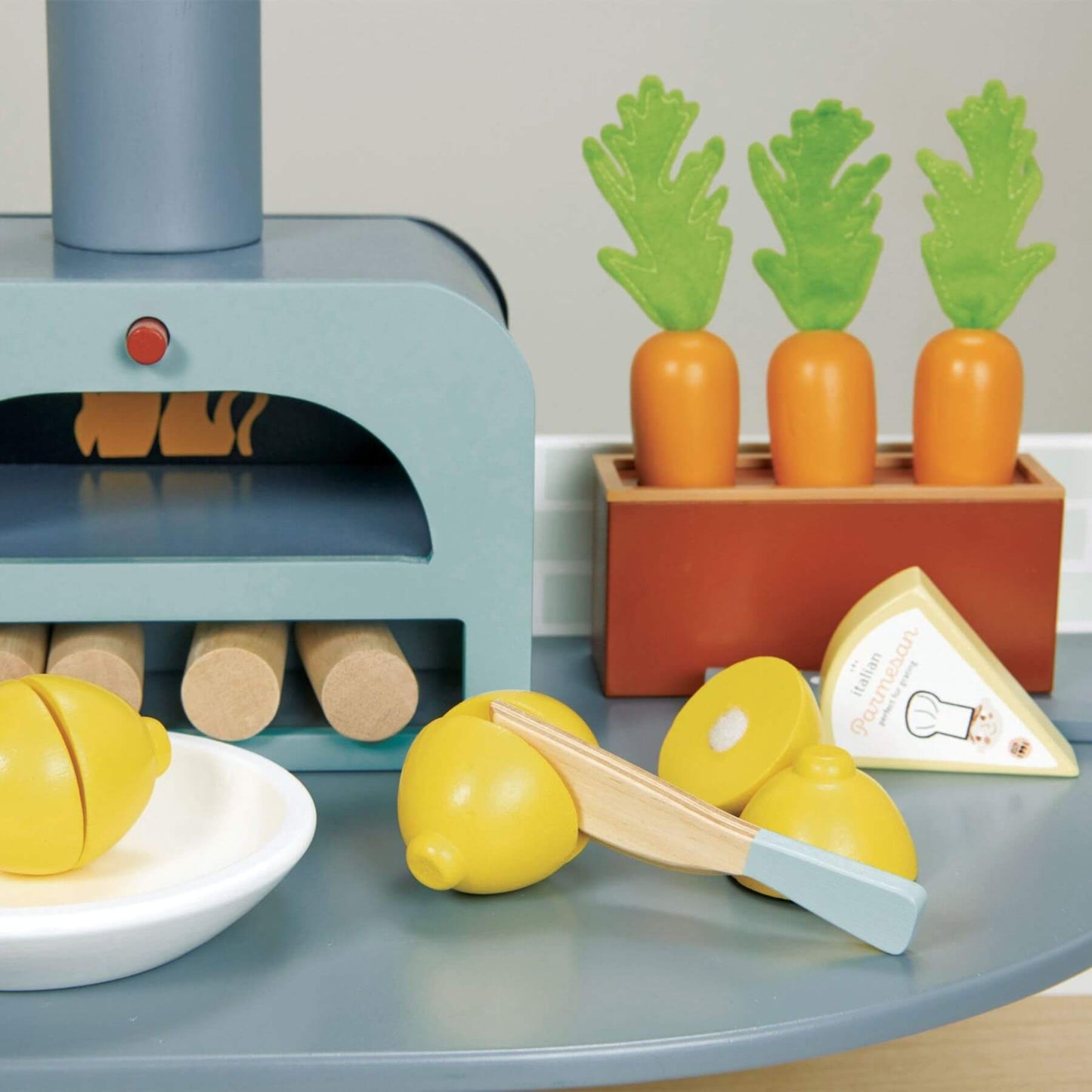 Toy kitchen set with lemon slices, knife, and carrots on a gray surface.