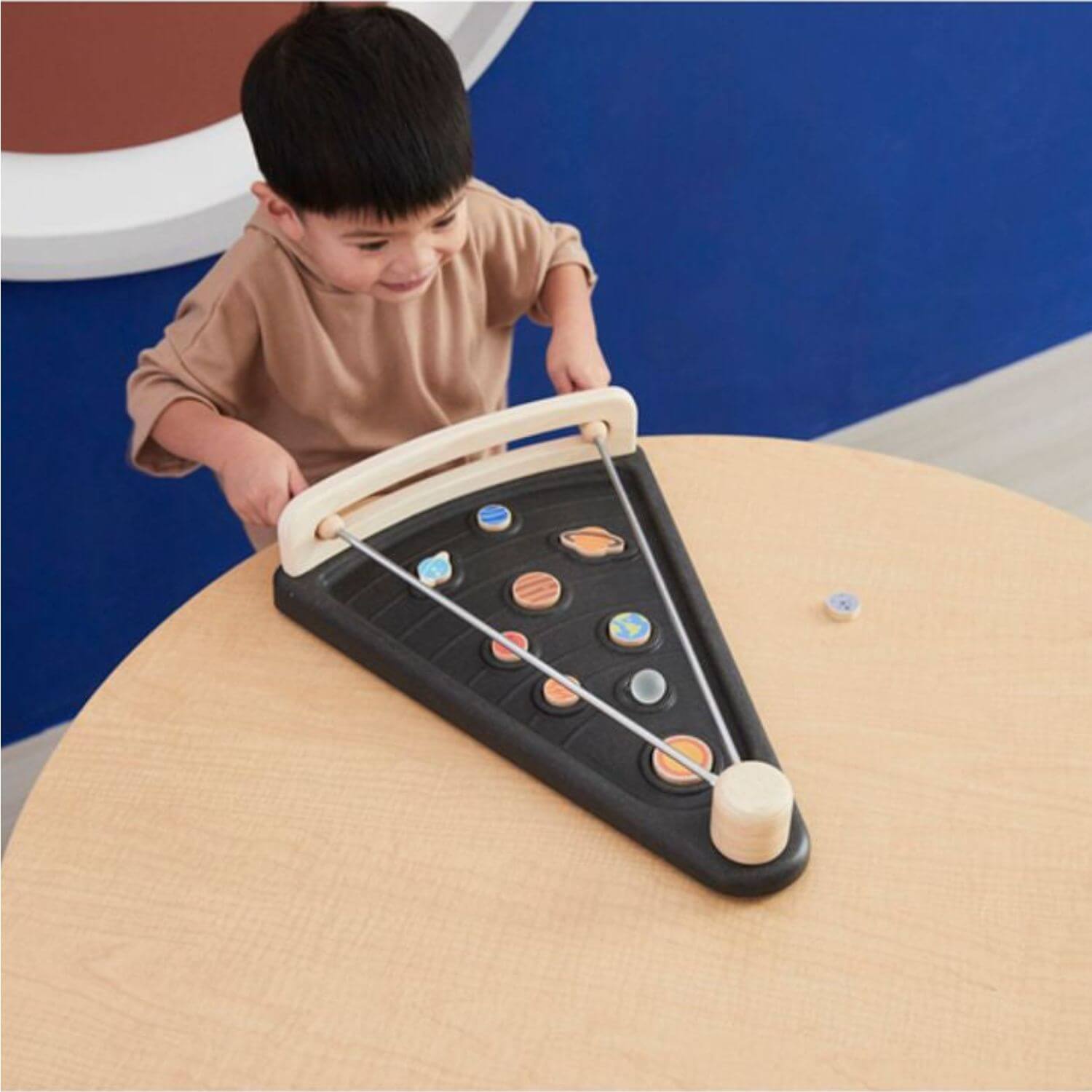 A young child  is playing with PlanToys Land The Planet on a light wood table.