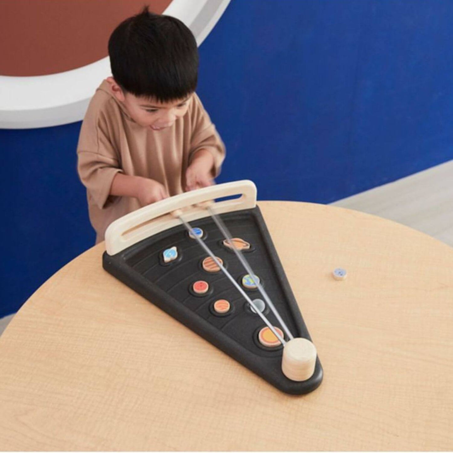 A young child is playing with PlanToys Land The Planet on a light wood table