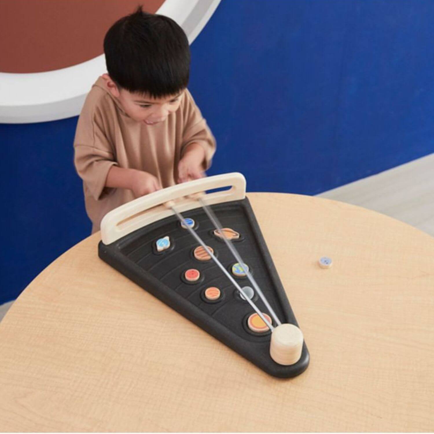 A young child is playing with PlanToys Land The Planet on a light wood table