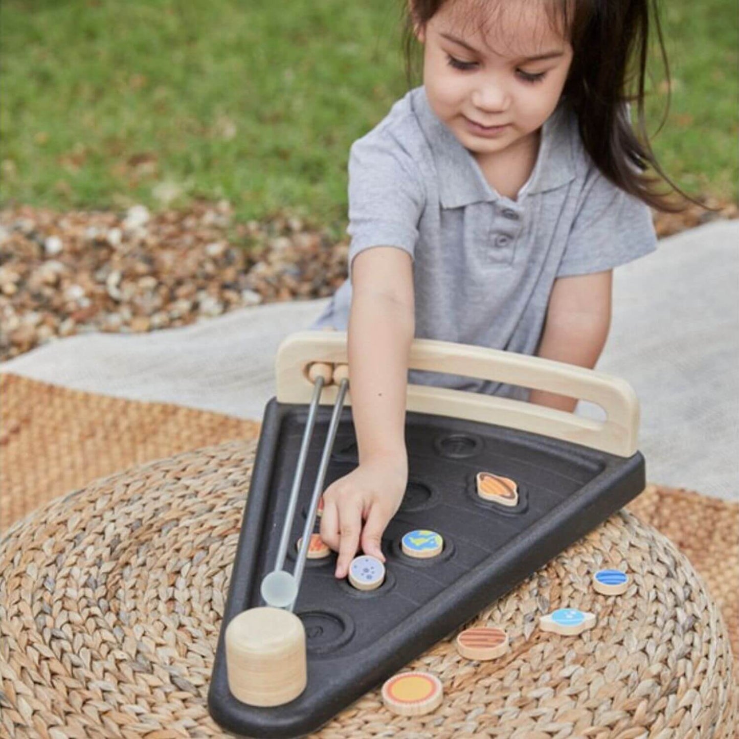 A young child is playing with PlanToys Land The Planet outdoors on a woven mat.