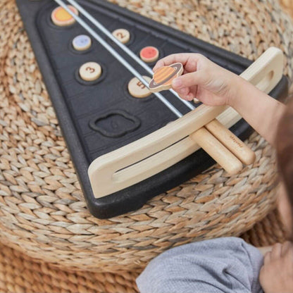 A child's hand holds a wooden planet toy over PlanToys Land The Planet, placed on a woven straw pouf.