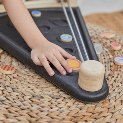 A child's hand pushes a wooden token along PlanToys Land The Planet, on a woven straw mat.
