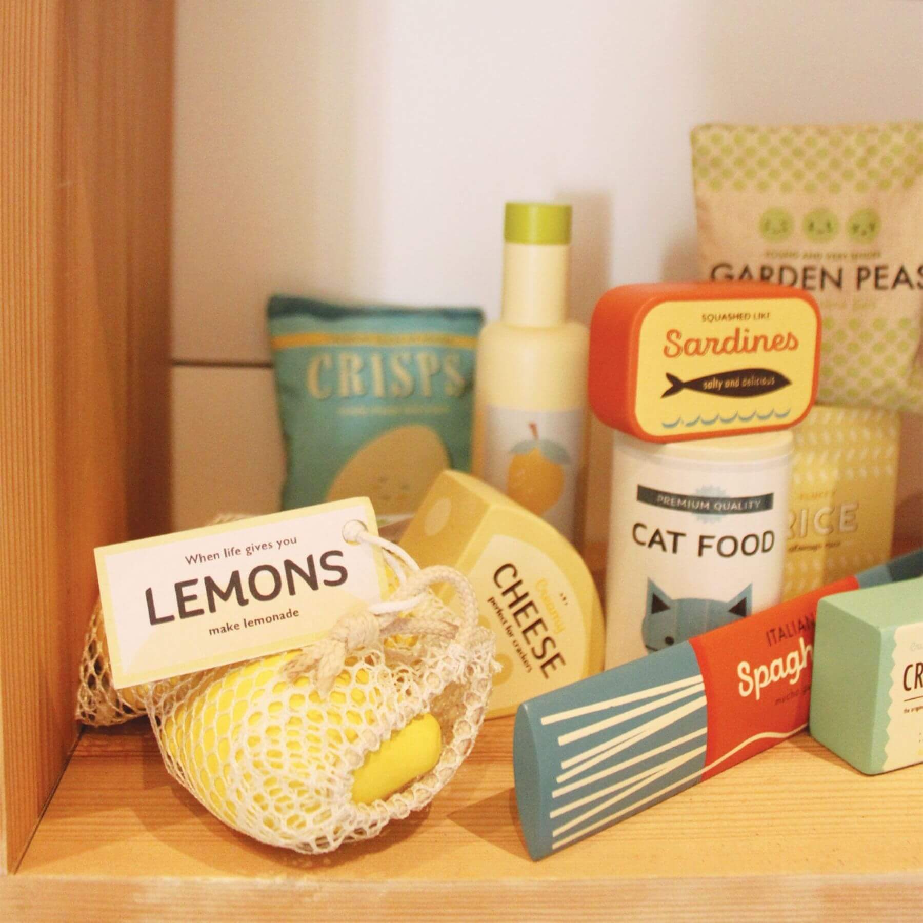 Assorted toy food items including lemons, cheese, cat food, and spaghetti on a wooden shelf.