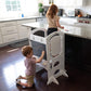 Girl Standing on Little Partners Limited Edition Learning Tower White, with a Boy Drawing on the Blackboard