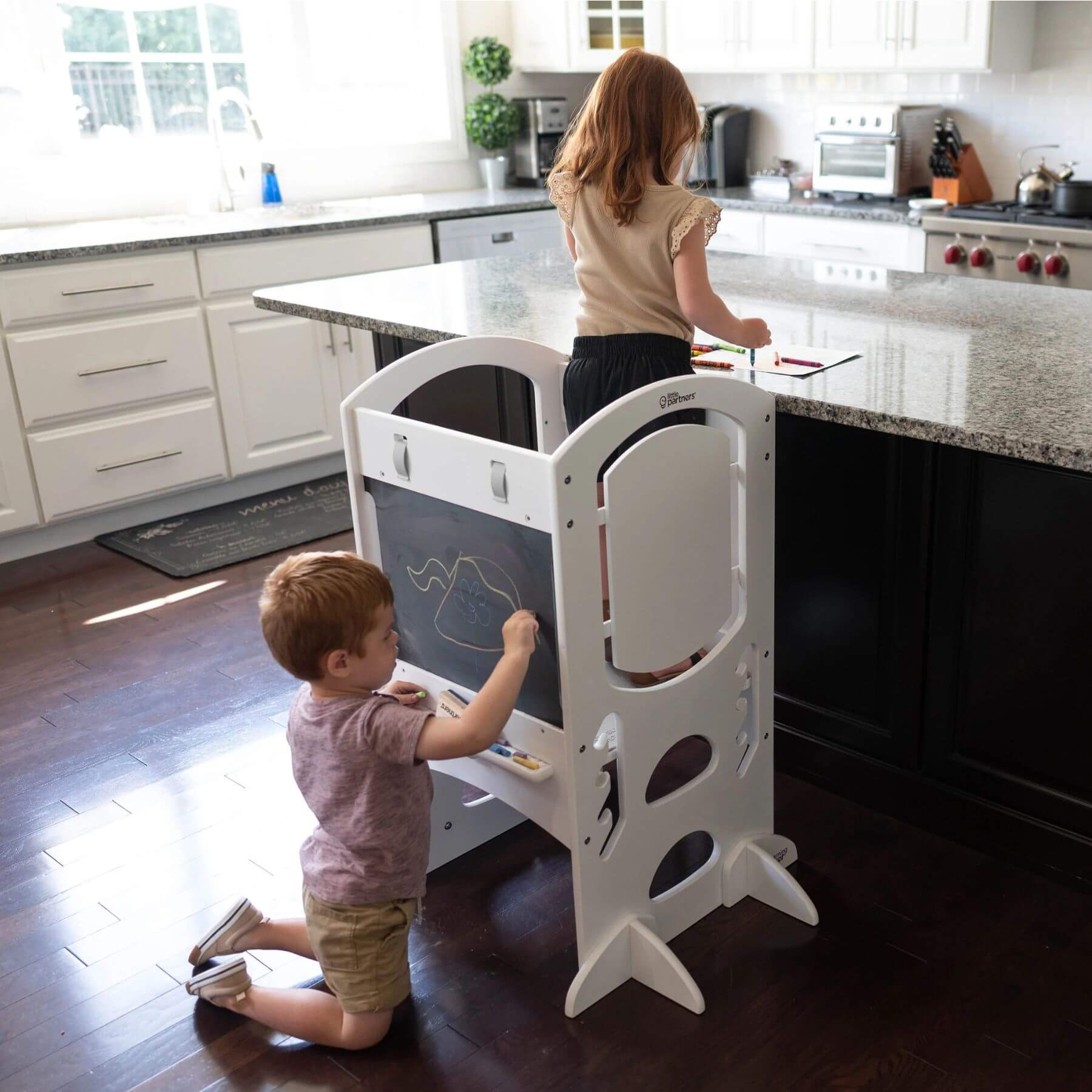 Girl Standing on Little Partners Limited Edition Learning Tower White, with a Boy Drawing on the Blackboard