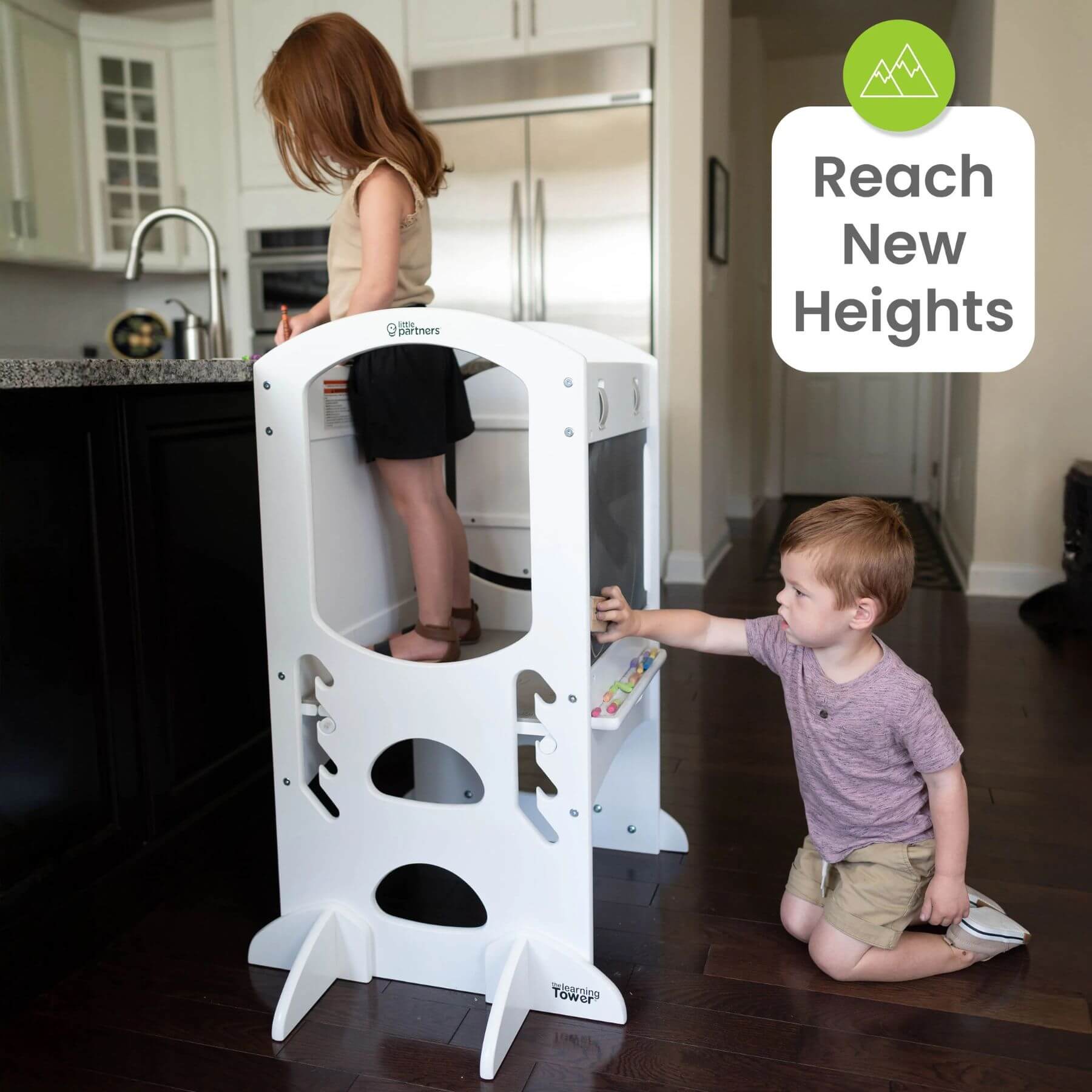 Girl Standing on Little Partners Limited Edition Learning Tower White, with a Boy Drawing on the Blackboard