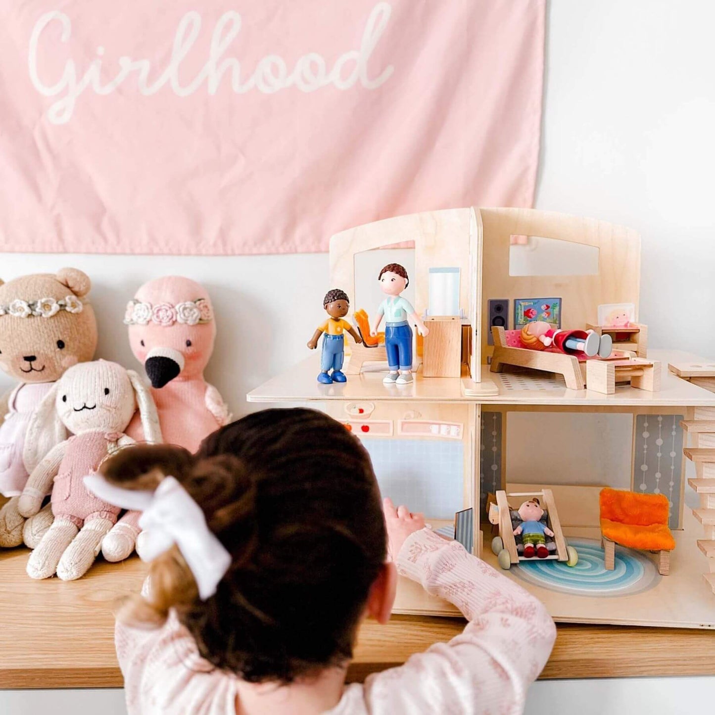 Child playing with Little Friends Dollhouse Town Villa with Furniture against a pink wall with 'Girlhood' text.