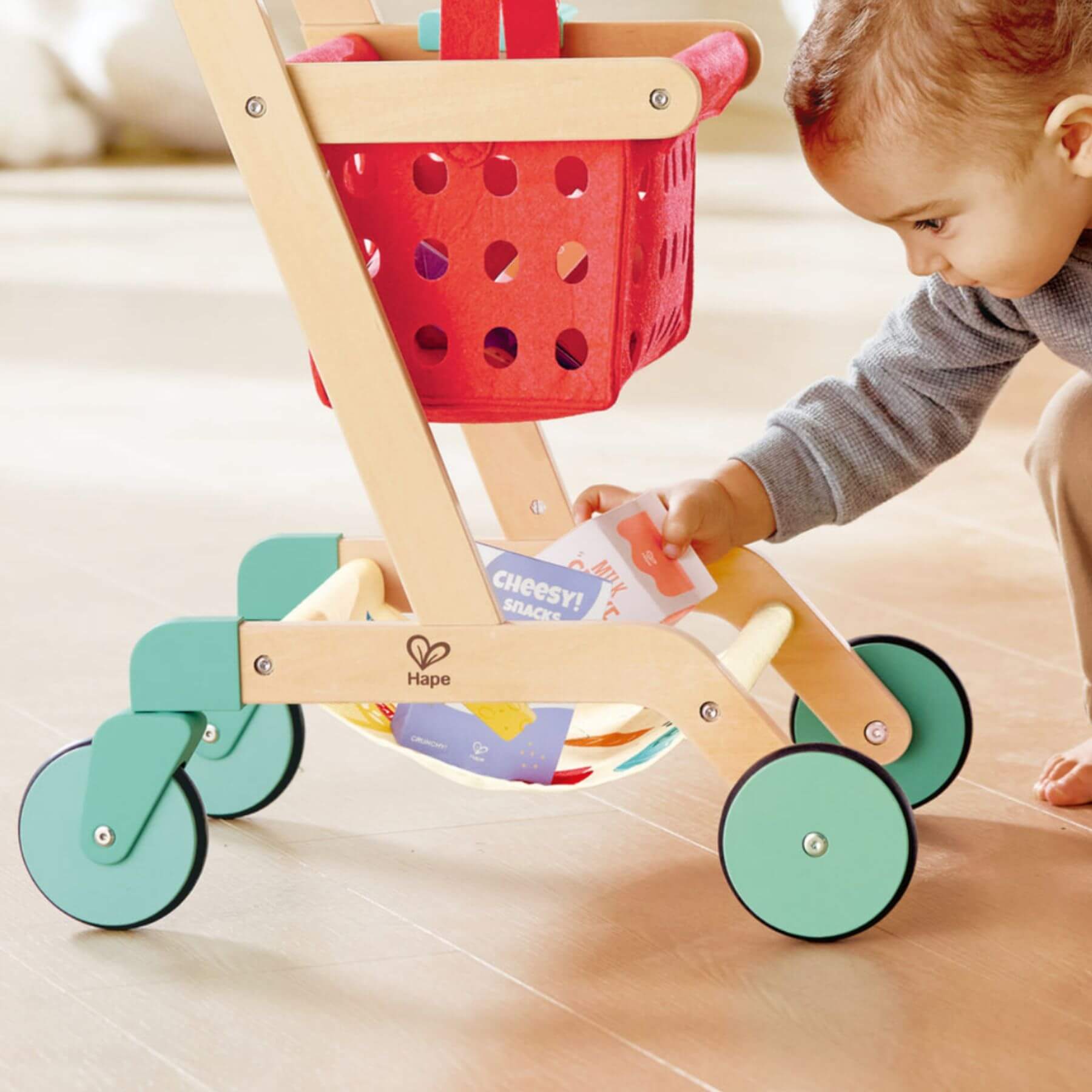 Child playing with Hape Little Shopper's Cart & Basket on a light-colored floor.