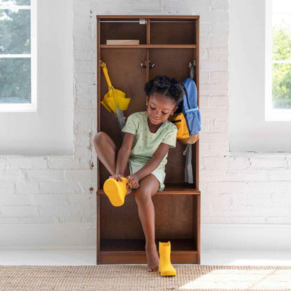 Child sitting on Little Partners Learn 'N Store Cubby with shoes and backpacks, in a room with white brick walls.